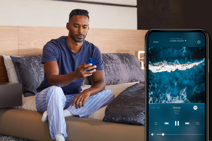 A man in pajamas on a bed, using a smartphone to control his home.